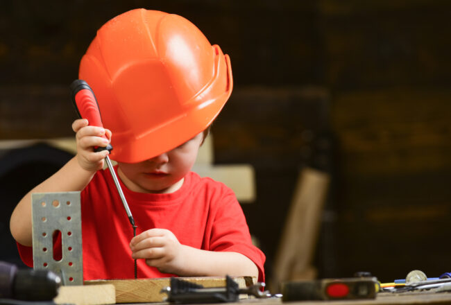 Boy play as builder or repairer, work with tools. Childhood concept. Kid boy in orange hard hat or helmet, study room background. Child dreaming about future career in architecture or building.
